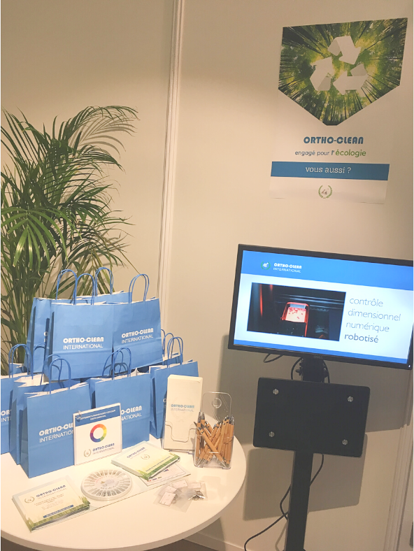 Zoom sur le stand avec sa pile de goodies Ortho-clean et sa vidéo expliquant la procédure de retraitement de l'entreprise.